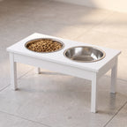 White elevated pet feeding station with two stainless steel bowls on kitchen tile