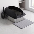 Stainless steel cat litter box with black lid, scoop and mat in a clean laundry corner