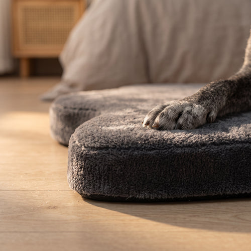 Close view of the plush grey top and low 2 inch profile of the orthopedic dog mat with a paw resting on it
