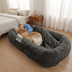 Dark grey CalmCurl human dog bed beside a bed in a bright bedroom